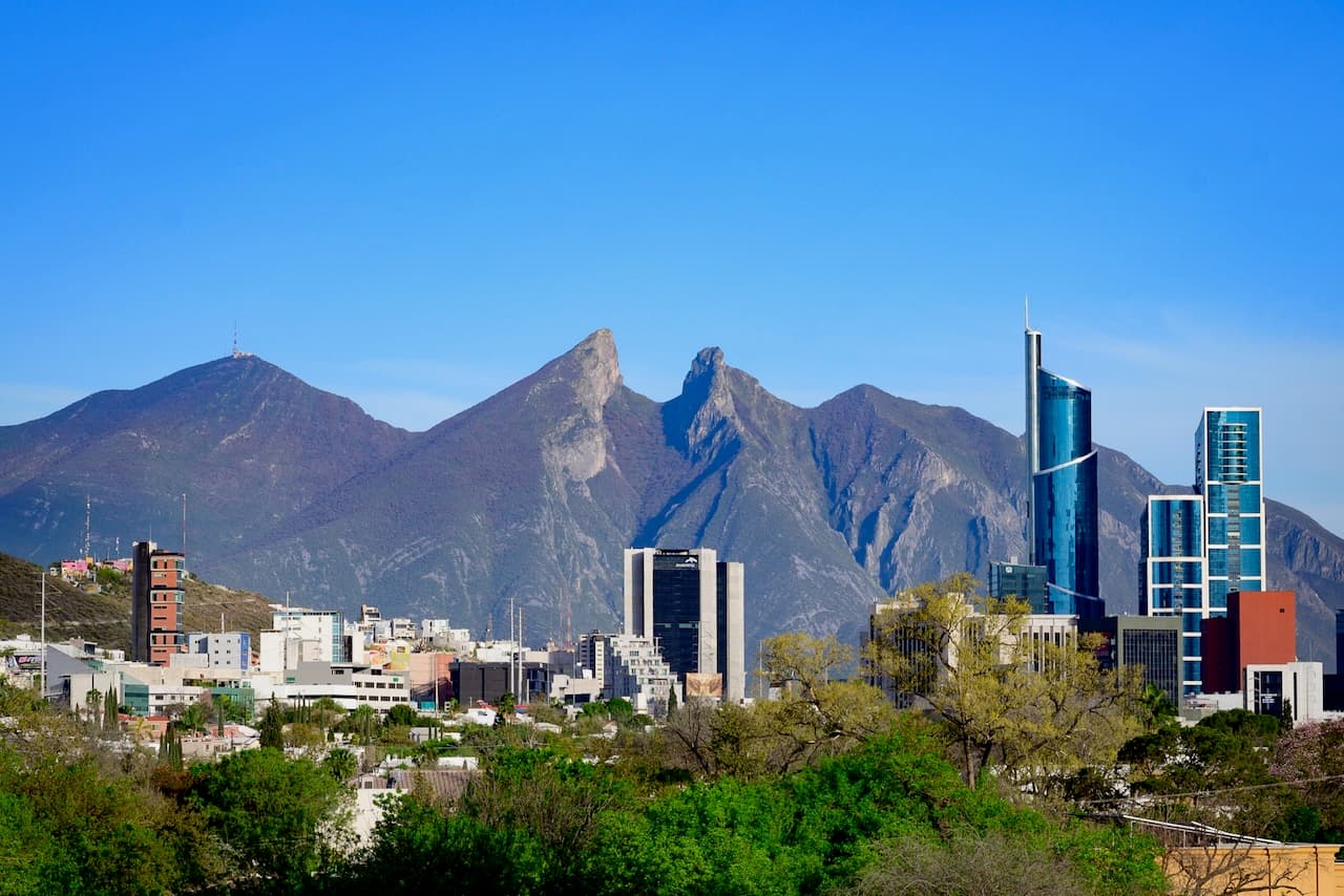 Vista panorámica de una ciudad moderna con edificios altos frente a montañas y un cielo despejado.