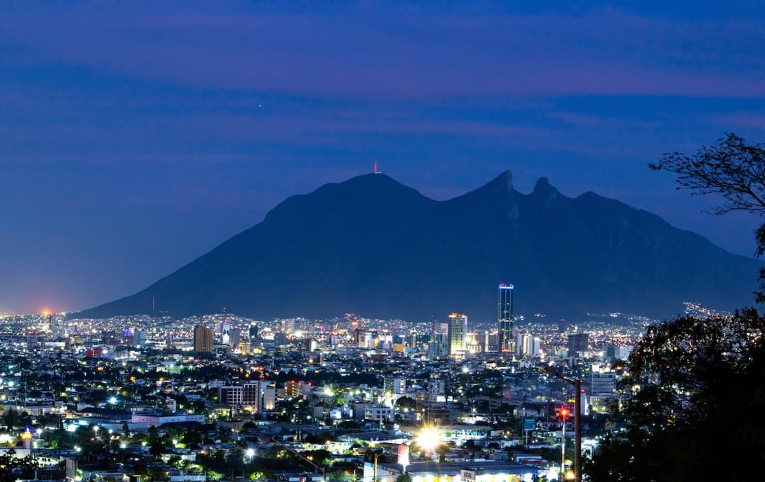 Ciudad de Monterrey con montañas al fondo, con un cielo azul y una luz natural.