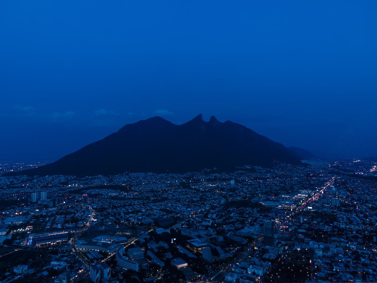 Vista panorámica de la ciudad de Monterrey al anochecer, destacando el cerro de La Silla y sus luces.