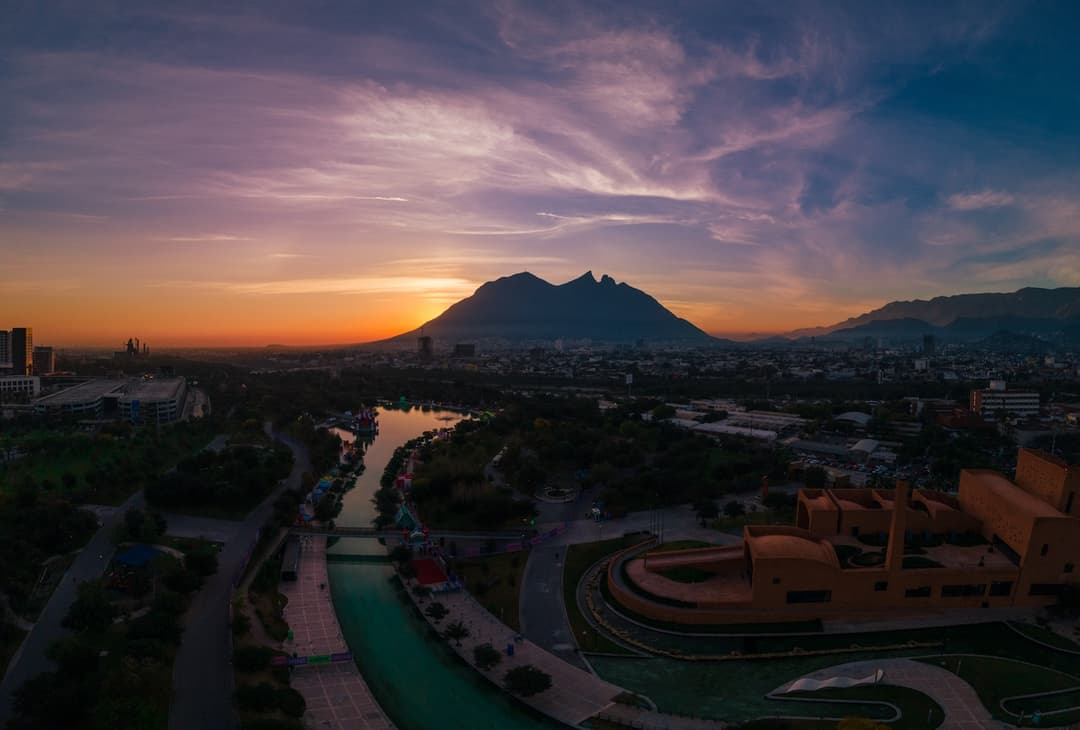 Ciudad de Monterrey con montañas al fondo, con un cielo azul y una luz natural.