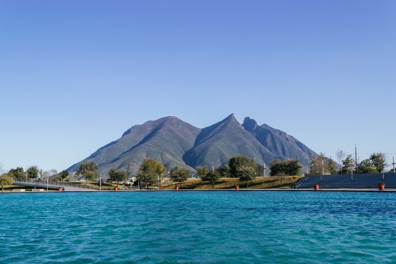 Montañas al fondo con un cielo despejado y un cuerpo de agua en primer plano.