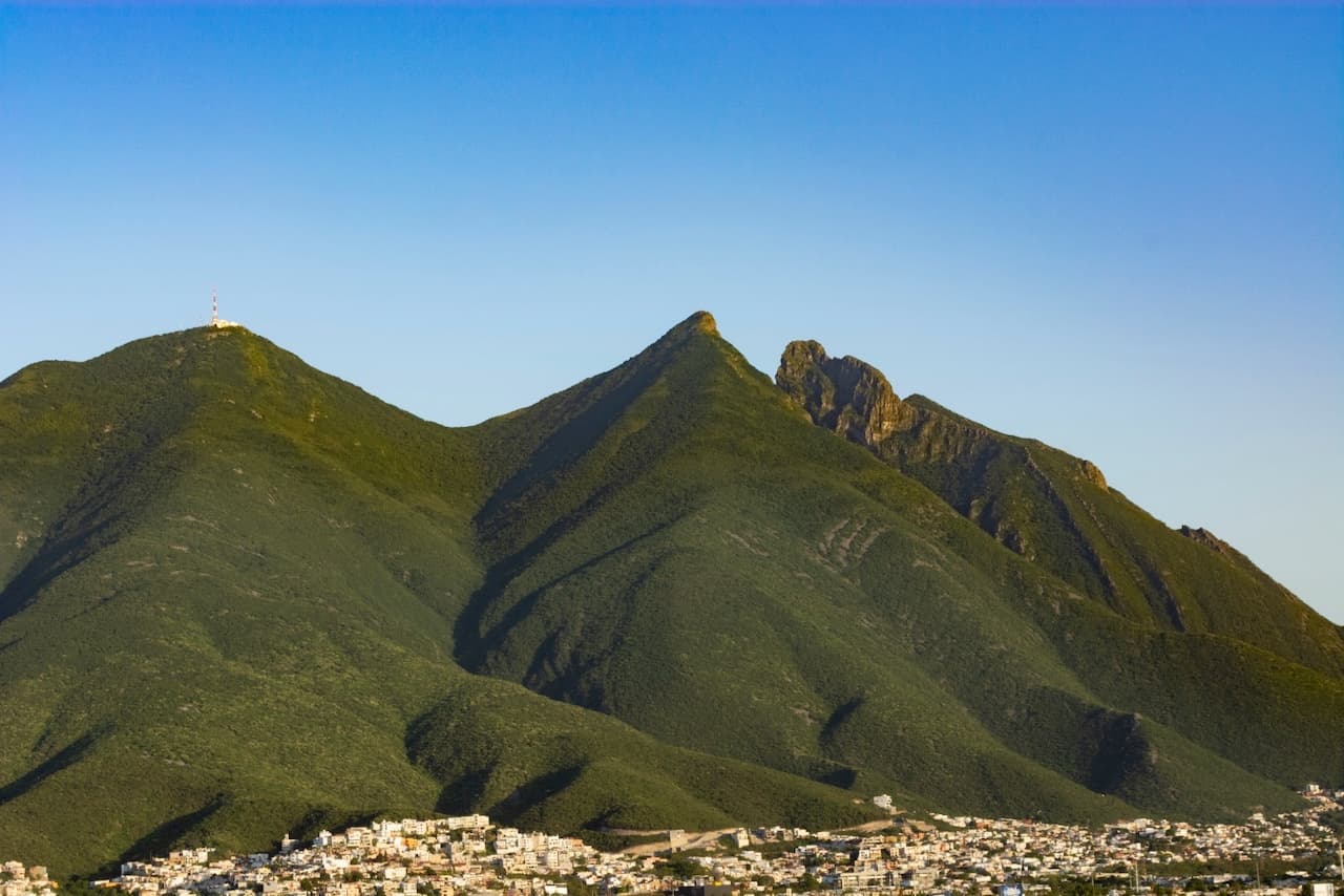 Montañas verdes con una antena en la cima y una ciudad visible al pie.