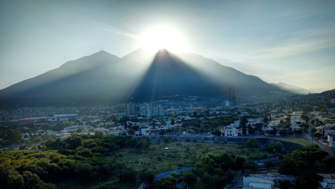 Ciudad de Monterrey con montañas al fondo, con un cielo azul y una luz natural.